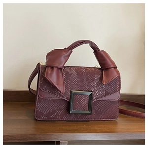 Detail of burgundy snakeskin texture handbag with metallic buckle and knotted handle