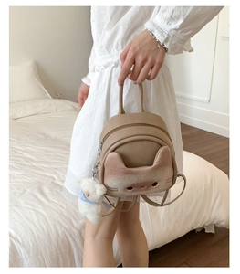Close-up of cute 3D cat face design and plush bear charm on beige mini backpack