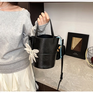 Close-up of black bucket bag with textured leather finish and floral pendant detail