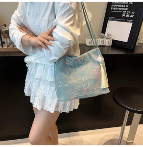 Detail of floral embroidery on light blue crossbody bucket bag with pearl tassel charm