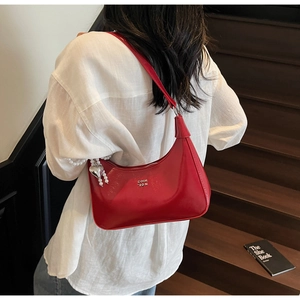 Close-up of a red patent leather hobo bag with a pearl heart charm and metal logo detail