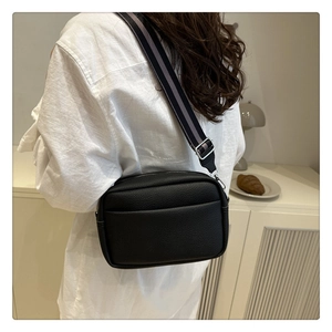 Close-up of black lychee grain crossbody bag with a sporty wide striped fabric strap