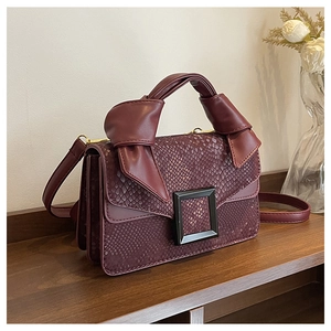 Detailed view of burgundy snake-pattern handbag with black square buckle on a wooden surface
