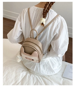 Detail of cute cat-ear mini backpack with plush ball charm shown on a model