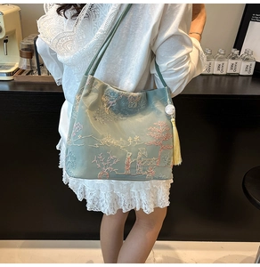 Detail of light green bucket bag featuring traditional Chinese embroidery and tassels