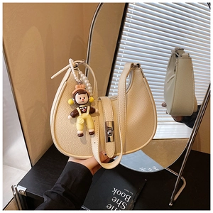 Detail of cream half-moon bag with lychee leather texture and pearl doll charm