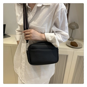 Close-up of black pebble leather crossbody bag with a wide striped fabric strap on a model