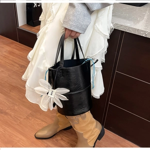 Detail of black bucket bag featuring a blue drawstring and white floral FUOR charm