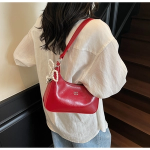 Detail of red patent leather dumpling bag featuring a large white pearl bow and silver logo