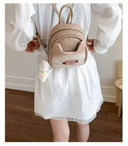 Detail of khaki cat-patterned backpack with plush charm on white lace dress
