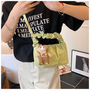 Detail of light green pleated underarm bag featuring a cute brown teddy bear pendant
