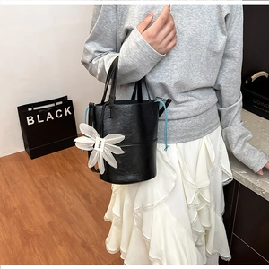 Detail of black pebbled leather bucket bag featuring a large white fabric flower charm