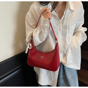 Close-up of shiny red patent leather bag with a pearl bow charm and logo detail