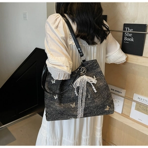 Detail of grey shoulder bag with silver butterflies and white lace bow pearl charm