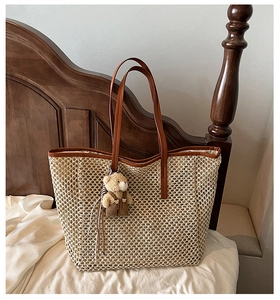 Détail d'un sac cabas en paille tressée beige avec anses en cuir marron et breloque ours