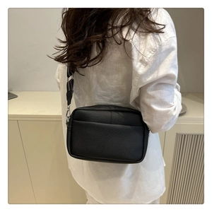 Detail of black lychee grain crossbody bag featuring an adjustable striped woven strap