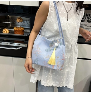 Detail of light blue bucket bag with floral embroidery and long yellow tassel decor