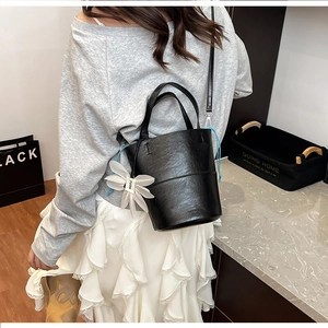 Minimalist black leather bucket bag with white flower charm shown in a lifestyle setting