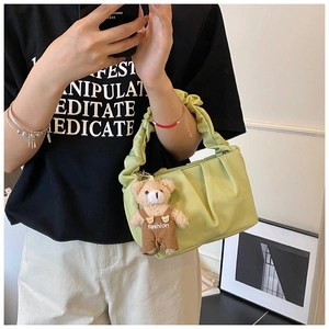 Detail of light green ruched handbag featuring a fashion plush bear charm and pleated strap