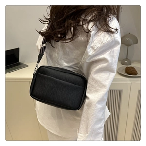 Detail of black litchi texture crossbody bag with wide striped fabric shoulder strap