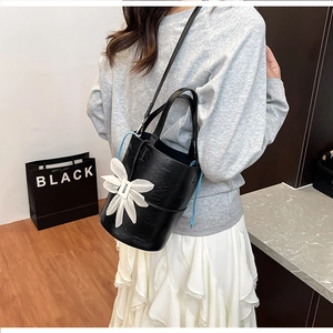Detail of black textured leather bucket bag with white floral charm and blue drawstring cords