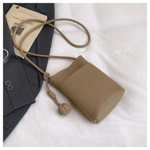 Close-up of khaki lychee grain leather crossbody bag with braided pendant and shoulder strap