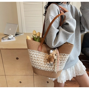 Detail of woven straw tote bag featuring contrast stitching and a cute bear plush pendant