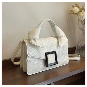 Close-up of white snakeskin embossed handbag with knot handle on a dark wooden surface