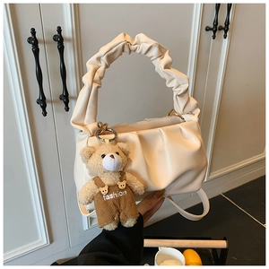 Detail of cream pleated handbag with ruffled handle and cute teddy bear charm pendant
