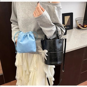 Detail of black leather bucket bag with a white bow charm and light blue drawstring pouch