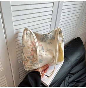 Detailed embroidery of Chinese pavilions and pine trees on an off-white bucket bag