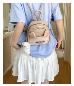 Beige cat-themed mini backpack with 3D ears and plush bear charm on a female model