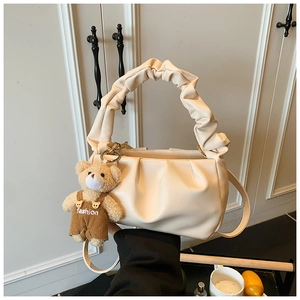 Detail of cream pleated hobo bag with a cute teddy bear pendant on white background
