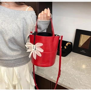 Detail of red bucket bag with natural leather texture and white floral charm on strap