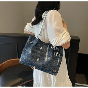 Detail of denim shoulder bag with butterfly appliques and delicate lace trimming