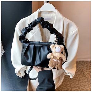Detail of black pleated shoulder bag with cute teddy bear charm and soft PU leather texture