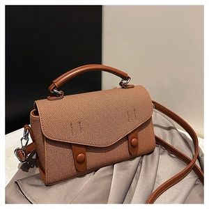Detail of a brown woven crossbody bag featuring retro messenger flap and leather straps