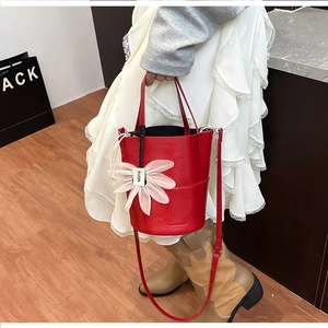 Close-up of a red textured bucket bag featuring a white flower charm and fine leather strap