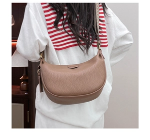 Detail of caramel pebbled leather saddle bag with wide striped textile strap and gold hardware
