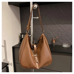 Detail view of large brown leather tote bag with metallic H-clasp in kitchen setting