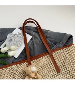 Détail du sac cabas en paille tissée avec anses en cuir brun et pendentif ours en peluche
