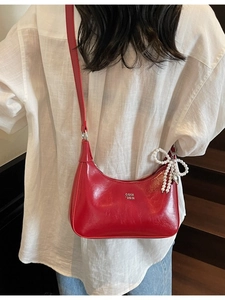 Red patent leather dumpling bag with pearl bow and adjustable shoulder strap worn by model