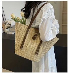 Detail of woven straw tote bag with brown leather straps and metallic buckle closure