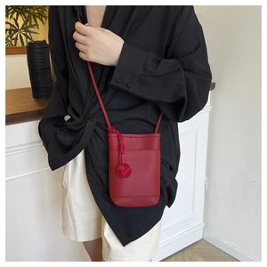 Detail of red mini crossbody bucket bag with litchi grain texture and tassel charm