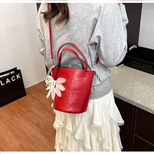 Detail of red leather bucket bag with white drawstring and flower charm on shoulder