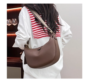 Brown leather crescent bag with wide geometric woven strap shown on model's shoulder