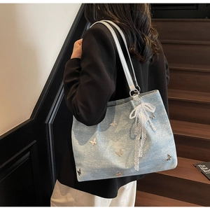 Detail of light blue shoulder bag with lace pearl bow and butterfly charms on denim fabric