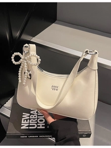 Cream hobo bag with pearl bow charm and silver logo on minimalist black book background