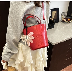 Detail showing red leather bucket bag with pink floral charm and fine embossed logo