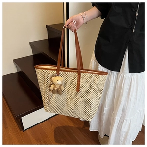 Détail d'un sac cabas en paille beige avec anses en cuir marron et pendentif ours en peluche